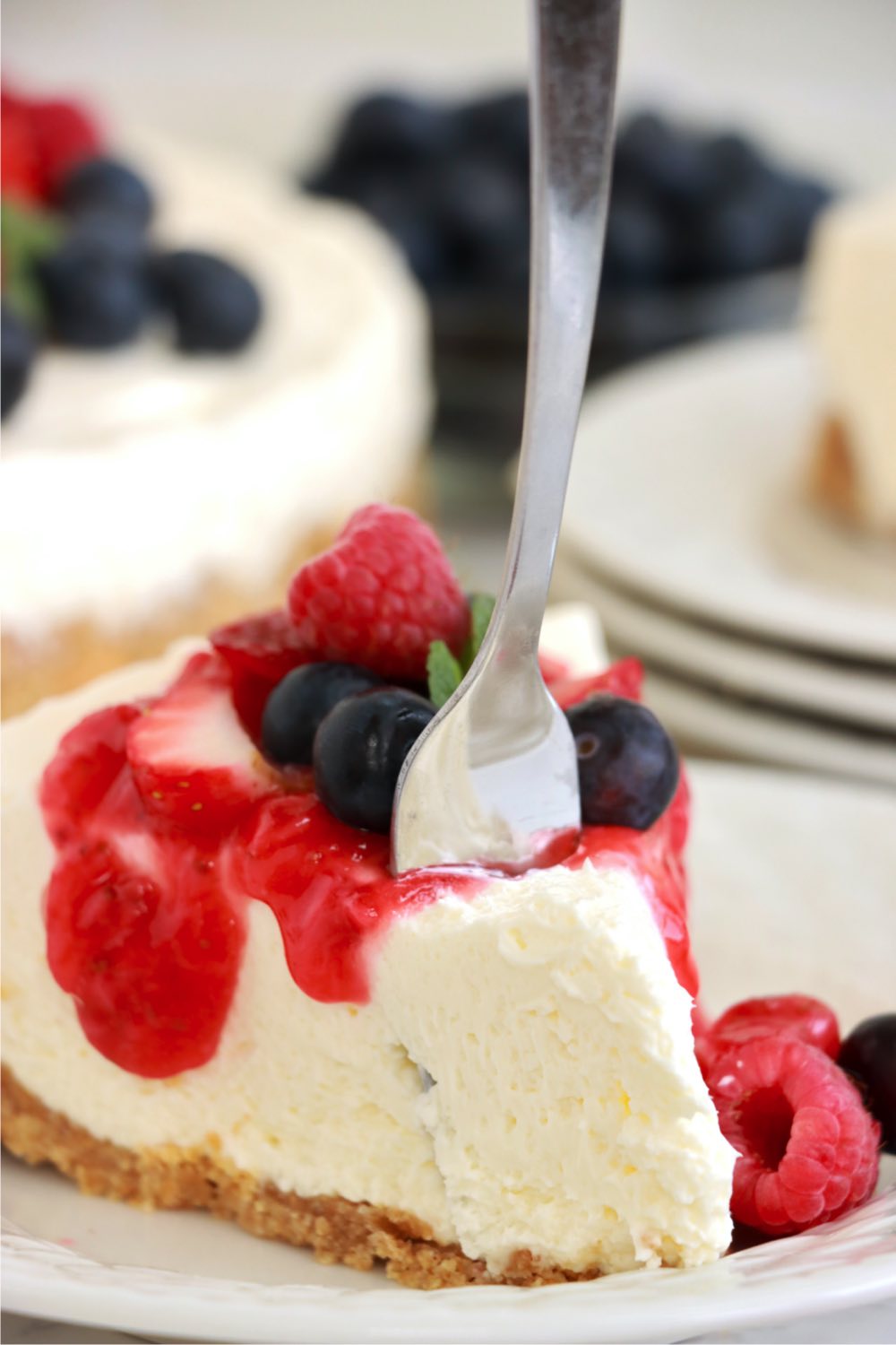 fork digging into a piece of cheesecake with strawberry sauce