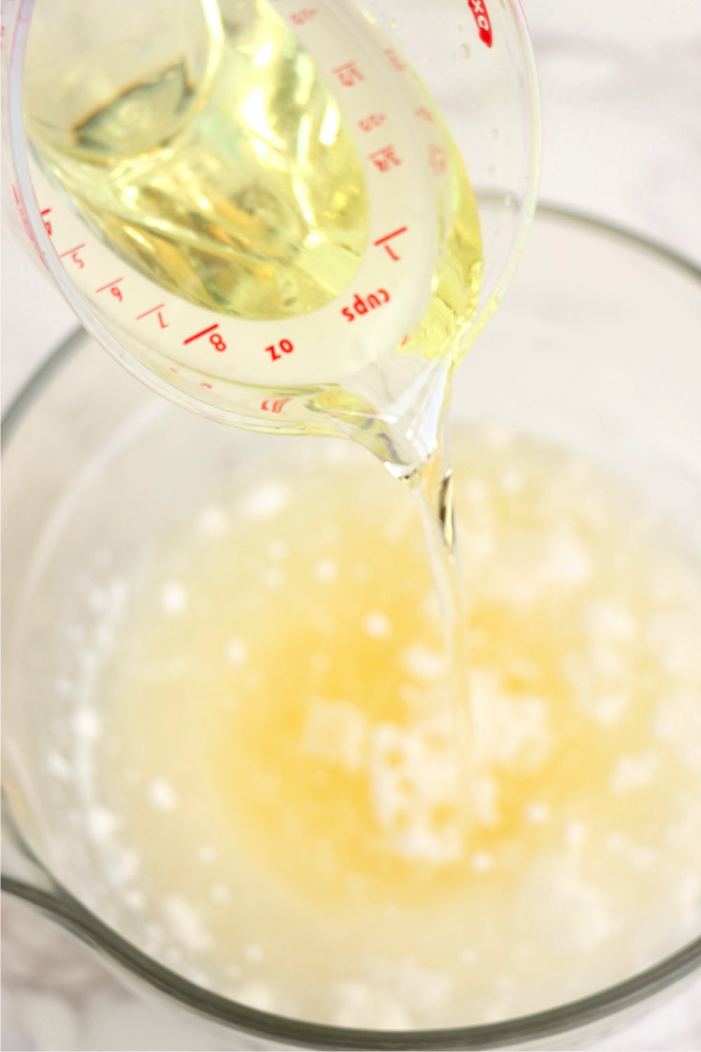 Pouring vegetable oil from a measuring cup into a glass bowl filled with cake mix and water.